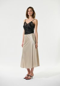 Camisole en satin noir avec dentelle, associée à une jupe midi en satin crème. Des sandales à lanières noires complètent le look.