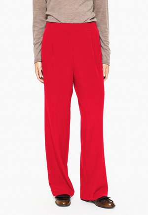 Red wide-leg trousers with a smooth texture, featuring front pleats and a high waistband, paired with a neutral long-sleeve top and brown shoes.