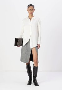 Camisa branca de botões, saia cinza dividida e botas pretas até ao joelho. Tecido suave, ajuste feito à medida, com um design elegante e uma grande mala castanha.