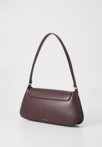 Sac à main Calvin Klein, cuir bordeaux, forme courbée, bandoulière amovible, texture lisse, et un rabat avant avec un détail de logo subtil.