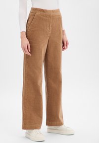 Brązowe spodnie sztruksowe o szerokich nogawkach z fakturą. Mają wysoki stan, boczne kieszenie oraz brzegi sięgające tuż nad buty.