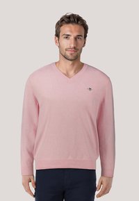 Roze V-hals trui van zacht materiaal, met lange mouwen en een klein geborduurd logo op de linkerborst. Getailleerd ontwerp.