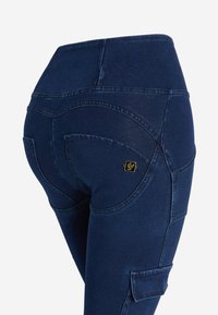 Jeggings blu scuro con vita alta, caratterizzati da dettagli di cuciture curve e un piccolo accent oro. Il tessuto sembra liscio ed elastico.