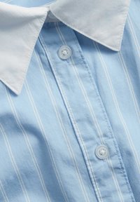 Ljusblå randig skjorta med vit krage, förskedd med två klara knappar och mjukt tyg. Vertikala vita ränder är synliga.