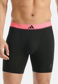 Svarta träningsshorts med ett midjeband i rosa och svart som har en logotyp. Tyget ser slätt och åtsittande ut, designat för komfort.