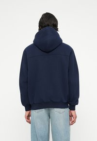 Sweatshirt à capuche bleu marine avec une coupe décontractée. Présente des poignets et un ourlet côtelés, un tissu doux et un subtil détail de couture au dos.