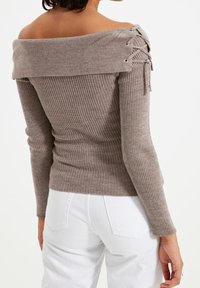 Pull côtelé à épaules dénudées en taupe avec détails lacés et œillets métalliques. Coupe ajustée, manches longues et texture douce.