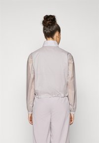 Lightweight, lavender jacket with a high collar, elastic cuffs, and a cinched waist. Features a textured pattern on the fabric.