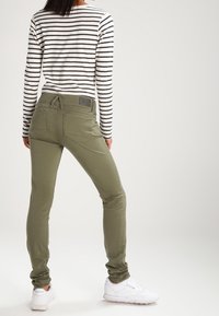 Gröna slim-fit byxor i bomullsblandning, med hög midja och bakfickor. Kombinerade med en svart-vitrandig långärmad topp.