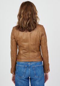 Brun læderjakke med en figursyet design, der har en mellemlang længde og diskrete sømdetaljer. Parret med blå denim jeans.