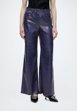 Woman wearing high-waist, wide-leg purple leather pants with subtle animal print, black sleeveless top, and pointed black heels with straps.
