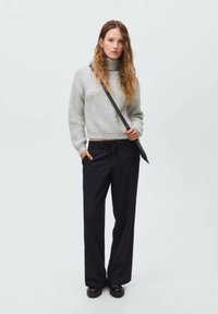 Maglione grigio a costine con collo alto, abbinato a pantaloni larghi a righe sottili scuri e calzature nere. Accessori minimi inclusi.