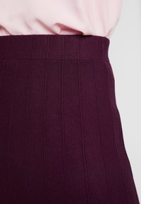 Ceinture violette côtelée d'une jupe, arborant des lignes verticales et une texture lisse, associée à un haut rose clair.