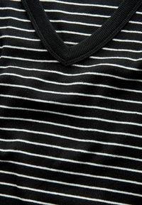 Melna v-veida blūze ar plānām baltām horizontālām svītrām. Materiāls šķiet mīksts, ir ribota apkakle un tam ir gluda tekstūra.