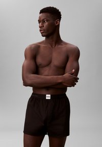 Czarne bokserki z logo Calvina Kleina na gumce. Model pozuje z założonymi rękami, prezentując materiał z bawełny oraz dopasowanie.