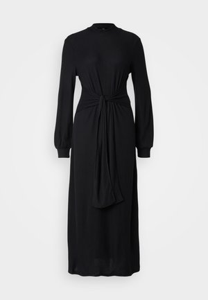 Vestido preto canelado com mangas longas, gola alta e detalhe de cintura nó. Silhueta vaporosa, feito de tecido texturado.