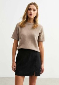 Suéter beige de manga corta combinado con una mini falda negra con una abertura lateral. Ambas prendas están confeccionadas en un suave y texturizado tejido.