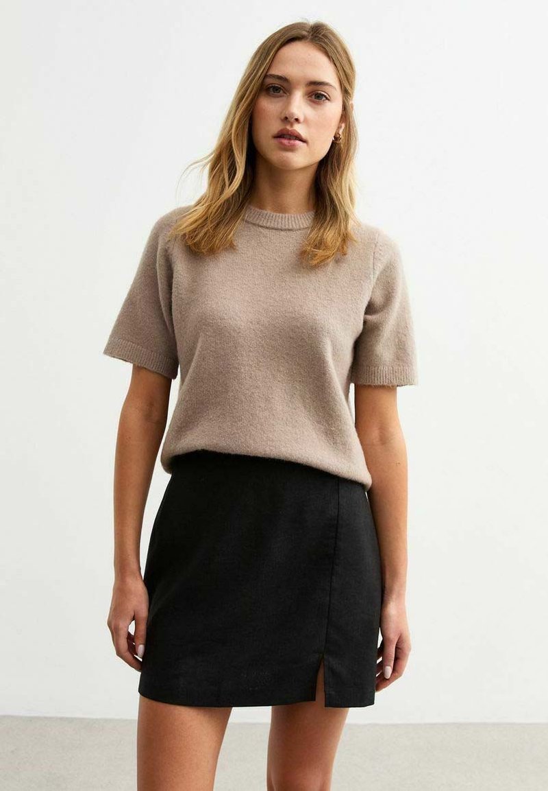 Beige kurzärmliger Pullover kombiniert mit einem schwarzen Miniröcke mit einem seitlichen Schlitz. Beide aus weichem, strukturiertem Stoff.
