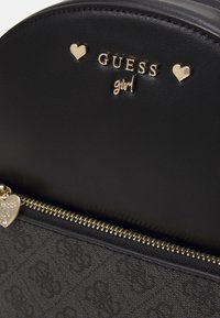 Sac à main synthétique noir avec des accents dorés, incluant un charme en forme de cœur. Le motif gaufré et la fermeture éclair ajoutent des détails texturés.