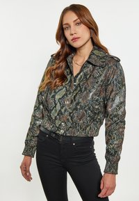 Jachetă cu imprimeu de șarpe, tăiată, dintr-un material shiny, texturat, cu închidere buton și guler mare; asortată cu blugi skinny negri.