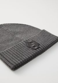 Gray knit beanie with a ribbed cuff. Features a textured pattern and a black logo accent on the side. Soft fabric.