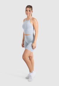 Lichtblauwe sportoutfit bestaande uit een cropped tanktop en high-waisted shorts, gemaakt van gladde, rekbare stof. Gekozen in combinatie met witte sneakers.