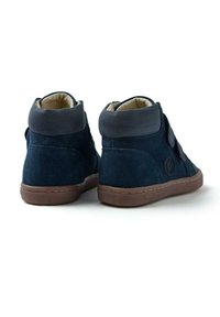 Zapatillas de ante azul marino de caña alta con un collar de cuero suave, banda de Velcro y suela de goma marrón. Forradas con tela de color claro.