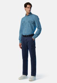 Camicia di jeans azzurro chiaro con due tasche sul petto, abbinata a pantaloni cargo blu scuro con una tasca laterale. Indossata con sneaker bianche.