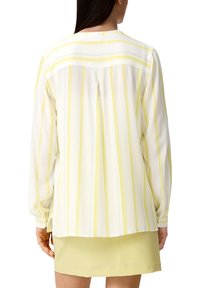 Blusa a maniche lunghe con righe verticali bianche e gialle, tessuto leggero, polsini con bottoni e dettaglio alla schiena.