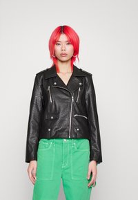 Svart lädermotorcykeljacka med dragkedjefickor och silverdetaljer, bärs med gröna cargobyxor. Har en krage och en kortad design.