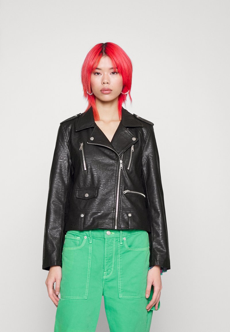 Svart lädermotorcykeljacka med dragkedjefickor och silverdetaljer, bärs med gröna cargobyxor. Har en krage och en kortad design.