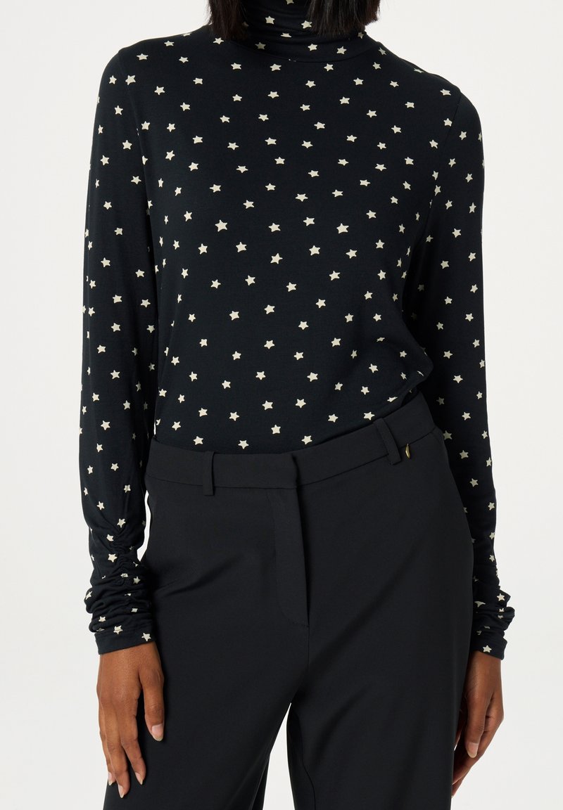 Svart långärmad polotröja med vitt stjärnmönster, tillsammans med högmidjade svarta byxor som visar midjan och armarna.