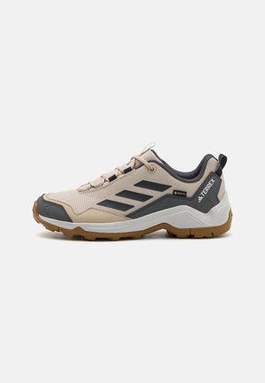Beiger und grauer Adidas Terrex Wanderschuh mit schwarzen Streifen, GORE-TEX-Label und brauner robuster Sohle, Seitenansicht.