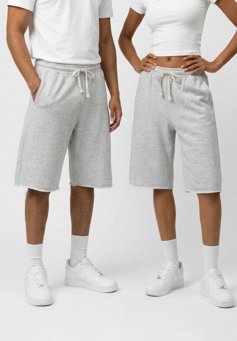 Deux personnes portant des shorts gris clair jusqu'aux genoux avec des cordons, des baskets blanches et des hauts blancs, debout côte à côte.