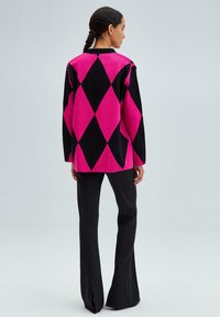 Maglione a motivo argyle rosa e nero con maniche lunghe e scollatura a girocollo, abbinato a pantaloni neri svasati. Texture liscia e vestibilità comoda.