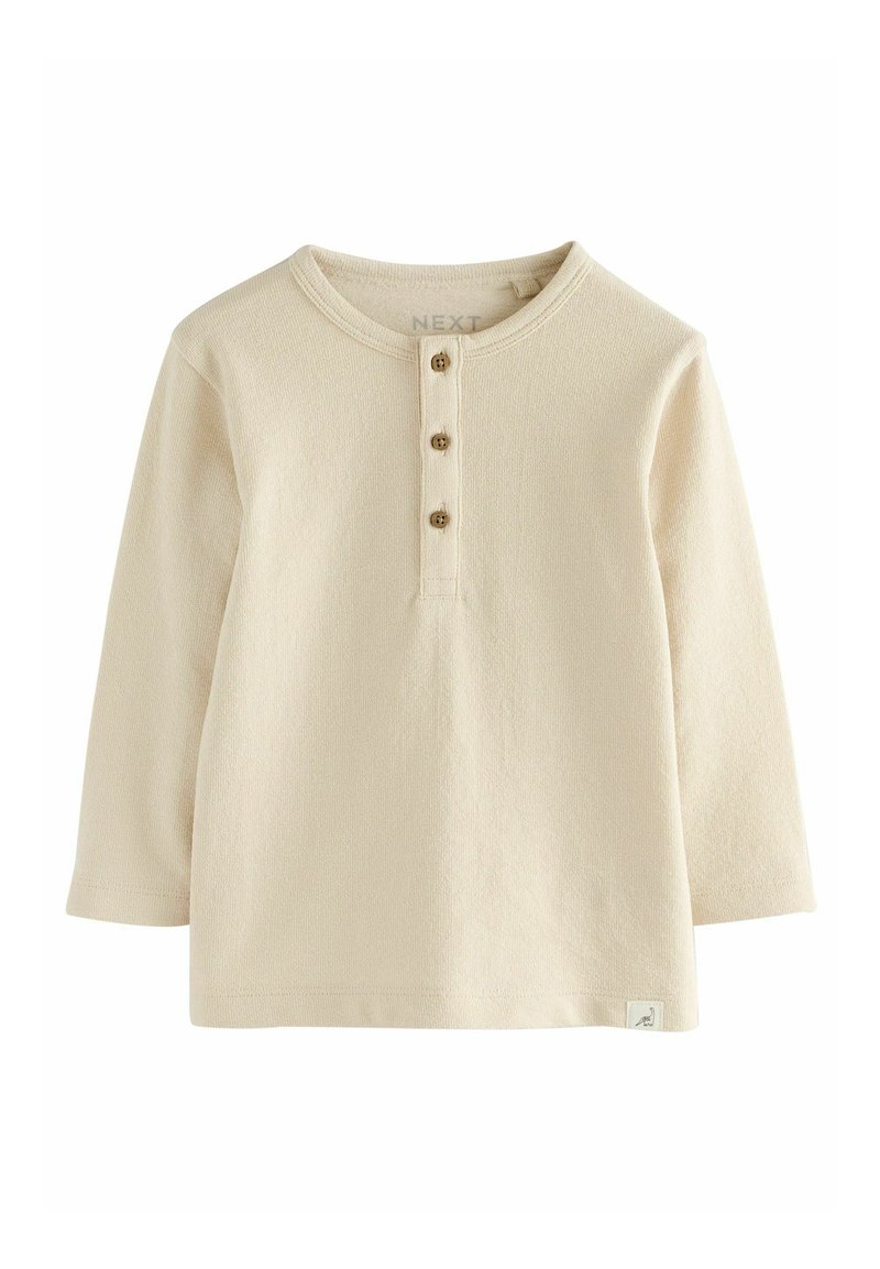 Chemise beige à manches longues en tissu texturé avec un col rond et une patte de boutonnage à trois boutons en bois. Étiquette à l'ourlet.
