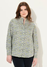 Camisa de manga larga de tejido ligero con un estampado floral en azul, verde y blanco; presenta un cuello alzado y cierre de botones.