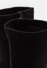 Bottines en daim noir à texture lisse, avec un bord supérieur arrondi et une fermeture éclair le long de la tige intérieure.