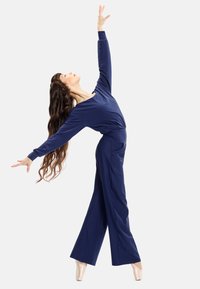 Marinblå jumpsuit i mjukt tyg, med långa ärmar, en omslagsdesign vid midjan och vida byxor. Dansaren poserar graciöst.