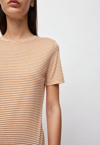 Camiseta de rayas de manga corta en marrón claro y blanco. Tejido suave con escote redondo clásico. Diseño ajustado, textura sin costuras.
