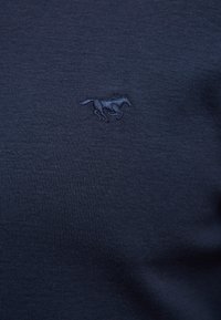 Tissu bleu marine avec un petit emblème de cheval brodé en fil bleu marine assorti, centré sur la surface.