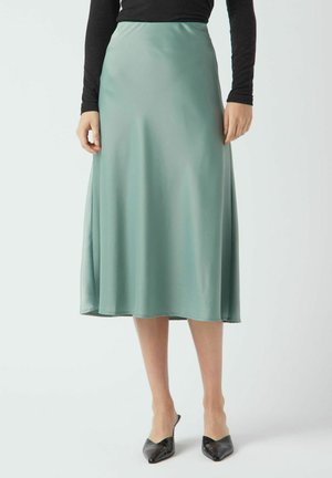 En satin, midi-længde nederdel i en blød grøn farve, med en glat tekstur og et flydende design, parret med sorte, spidse sko.