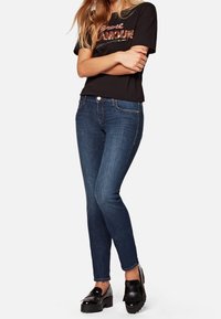 Mörk tvättade skinny jeans med midjehöjd och subtila blekningar, ihop med en svart t-shirt med "Glamour" i paljetter. Svarta platåskor.