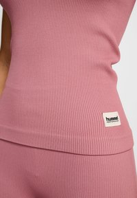 Różowy top na ramiączkach z prążkowanym wzorem o dopasowanym kroju, z białą metką logo "hummel" na dolnym lewym boku. Gładka tekstura materiału.