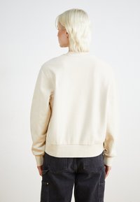 Cremefarvet sweatshirt med rund halsudskæring, ribbede manchetter og nederkant. Blødt, tekstureret stof med en afslappet pasform og enkle design detaljer.