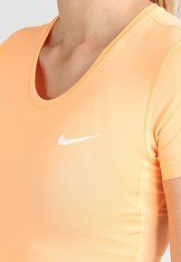 Oranssi urheilupaita, joka on valmistettu joustavasta kankaasta, jossa on pyöreä kaula-aukko, lyhyet hihat ja valkoinen Nike-swoosh-logo rinnassa.