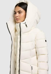 Witte pufferjack met een hoge kraag, oversized capuchon, geborduurd ontwerp, zwarte rits en zijpatch. Zachte textuur en warme isolatie.