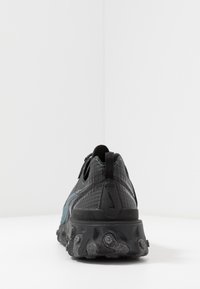 Svart och teal sneakers med texturerad mesh-överkonstruktion, flexibel sula och framträdande gummiklack. Har en dragflik vid hälen för enkel påtagning.