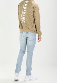 Beige polka dot sweatshirt with white lettering on the back, paired with light blue slim-fit jeans and white sneakers.