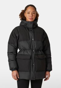 Zwarte gewatteerde jas met een trekkoord capuchon, knoopsluiting, twee grote voorzakken en elastische manchetten. Heeft een getailleerde taille voor een goede pasvorm.